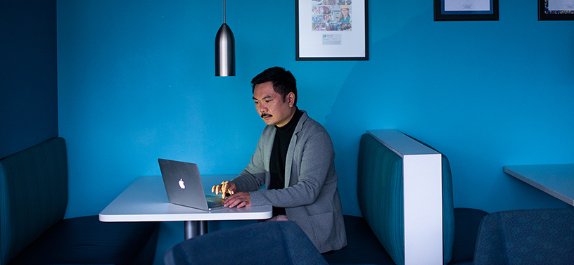 Dr Matthew Chow sits at a table working on a laptop