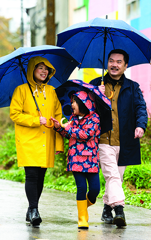 Dr Matthew Chow and his family walk in the rain under umbrellas
