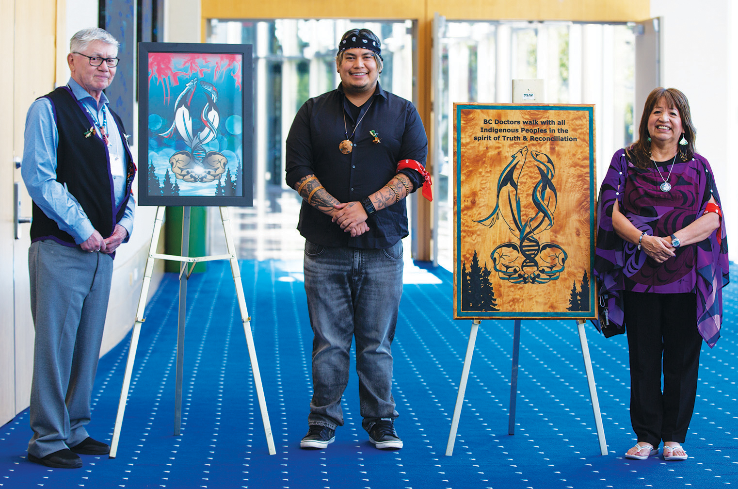 BC Indigenous artist sɬə́məxʷ Rain Pierre stands with the artwork The Light of Irene and his parents.