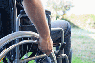A man sits in a wheelchair, looking out at a lake