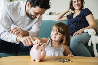 A couple sits with their small child with a piggy bank in front of them
