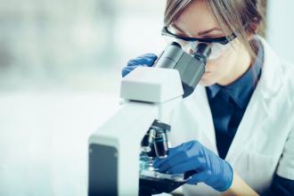 A scientist looks through a microscope in a lab