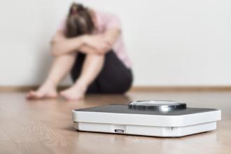 A woman sits beside a scale, with her head in her hands