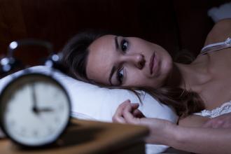 A woman lies awake in bed, staring at the clock