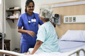 A patient sits on a hospital bed, talking to a doctor
