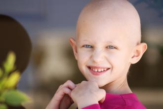 A girl who has lost her hair from cancer smiles at the camera