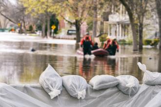 Rescuers traverse a flooded street by boat; sandbags are seen in the foreground