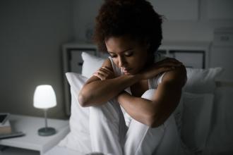 A woman with depression sits in bed with her hands around her knees