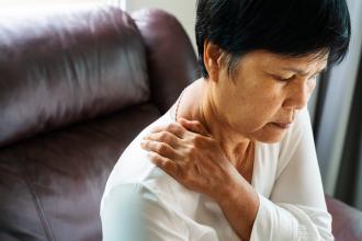 A woman puts her hands on her neck in pain