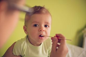 A doctor holds a swab at a baby's open mouth.