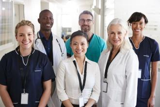 A multiracial group of smiling hospital staff in a hallway faces the camera.