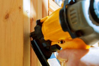 A construction worker uses a nail gun in close-up.