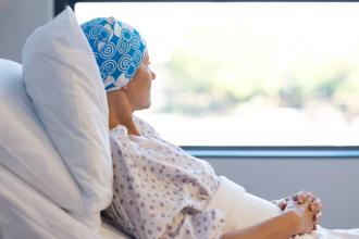 A patient with cancer sits in bed, looking out the window