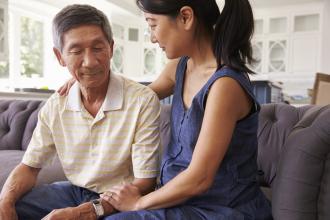 Adult daughter with an arm around her father on the couch