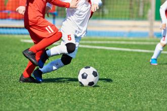 Two youth in uniforms playing soccer