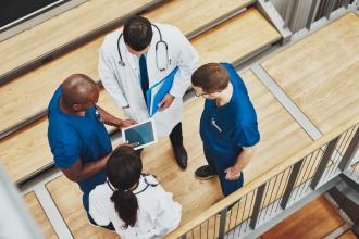Multiracial medical team standing together around a tablet, overhead view