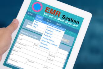 A doctor holds a tablet with an electronic medical records interface on the screen