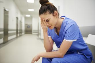 A doctor wearing scrubs sits in a hallway looking distressed