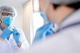 A doctor puts on a mask, looking in a mirror