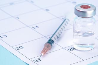 A vial of vaccine and a syringe sit on top of a calendar page