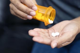 A hand is shown taking two pills out of a prescription bottle