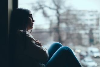 A teen sits down, leaning against a wall, looking sad