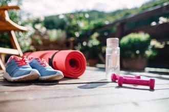 Running shoes, a yoga mat, dumbbells, and a water bottle are set out on a deck