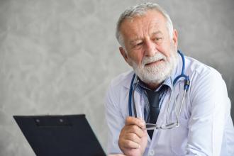 A senior doctor sits in front of a computer, looking reflective