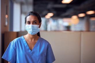 A doctor wears a mask and scrubs, looking determined