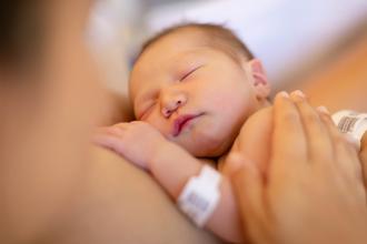 A baby wearing a hospital wristband sleeps on its mother’s chest