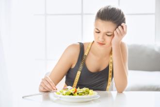 A person eats a salad, looking unhappy