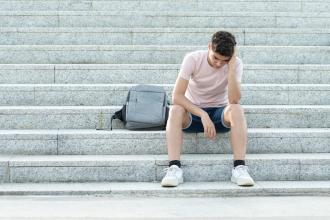 A teenager sits on a concrete staircase with his head in his hands