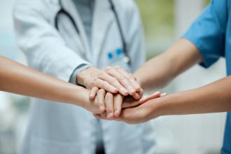 A group of health care professionals stand in a circle with their hands stacked on top of each other