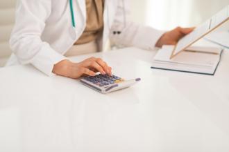 A doctor reviews paperwork and uses a calculator