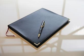A notebook sits on a table, with a pen on top of it