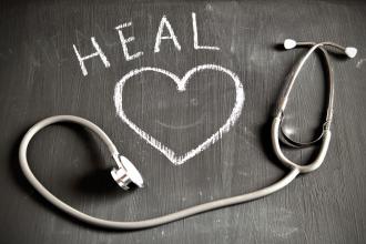 A stethoscope sits on a chalk board with a heart and the word "HEAL" written on it
