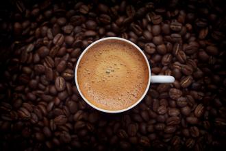 A top-down photo of a cup of coffee surrounded by coffee beans