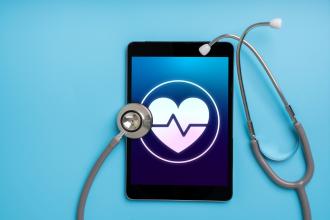 A stethoscope sits on a tablet with a heart shape on the screen