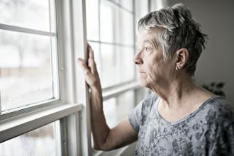 A senior stands at the window, looking unhappy