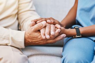 A doctor sits next to a patient, holding their hands.