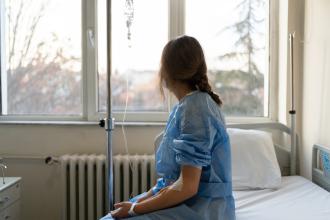 A patient sits on a hospital bed, looking out the window.