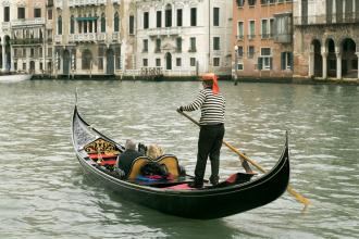 A gondolier standing in the back of a boat, with two passengers in the front.