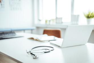 A laptop and stethoscope sitting on an otherwise empty desk.