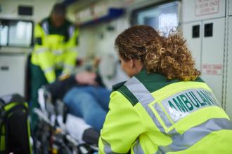 Two paramedics lift a patient on a stretcher into an ambulance.