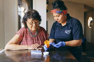 An Indigenous health care worker talks to an Indigenous patient while holding medication.
