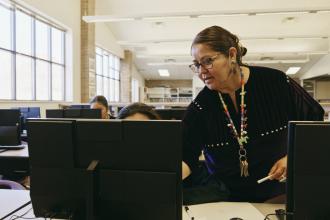 An Indigenous instructor helps students in a computer lab.