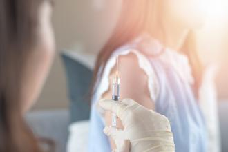 Female doctor's gloved hand holds syringe with woman in background