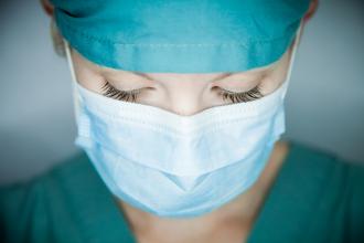 A doctor wearing a mast closes her eyes in exhaustion