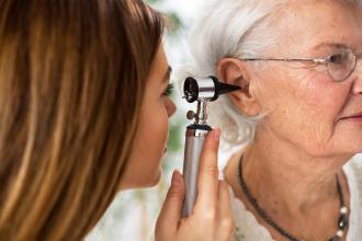 Doctor holding otoscope and examining ear of senior woman