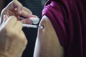 Doctors gloved hand giving needle to young man's upper arm